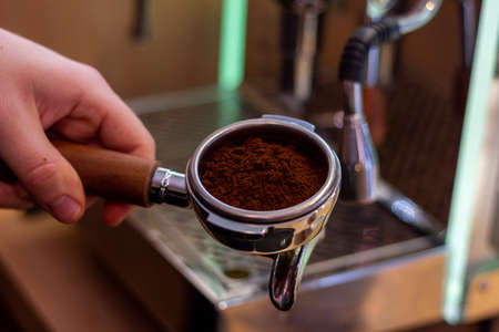 A portrait of a barista holding a coffee portafilter with fresh coffee grounds in it ready to make some coffee in the coffee machine.の写真素材