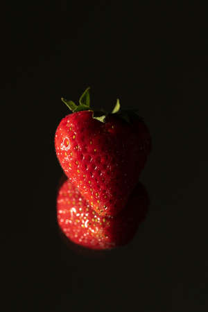 A portrait of a strawberry in the dark with its reflection in a mirror.の写真素材