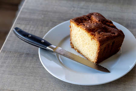 A portrait of a apple pound cake on a white plate on a wooden table with a bread knife on the plate. It is made from apples, sugar, flour, eggs and butter and is baked in an oven.の写真素材