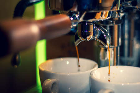 A portrait of the nozzle of a coffee machine. Freshly made and hot coffee is being made out of...