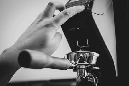 A portrait of a barista pressing the button of a coffee grinder to fill a portafilter full of freshly grinded coffee grounds from fresh coffee beans.の写真素材