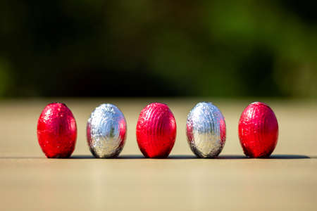 A portrait of chocolate easter eggs wrapped in tin colorful foiln standing up on a table ready to be found and eaten by children on their easter egg hunt.の写真素材