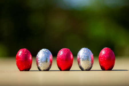 A portrait of five colorful and shiny easter eggs in their wrapping standing up on a table for children to find.の写真素材