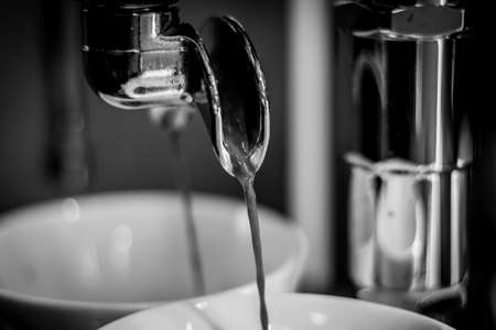 A black and white portrait of fresh hot coffee running out of the portafilter of a coffee machine.の写真素材