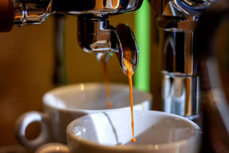 A portrait of freshly made coffee running out of a portafilter from a coffee machine into two coffee mugs.の写真素材