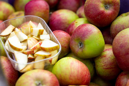 A close up portrait of a wooden crate full of apples at a local market. There is a plastic tray full of apple slices to taste the fruit to make the product more appealing to the customers.の写真素材
