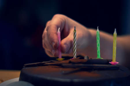 A portrait of a person putting candles on a chocolate birthday cake to blow out and celebrate. Only the hand is visible.の写真素材