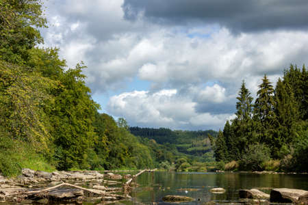 A portrait of the semois river in the vresse sur semois region in the Ardennes in Belgium. The river is surounded by hills and a forest at both sides.の写真素材