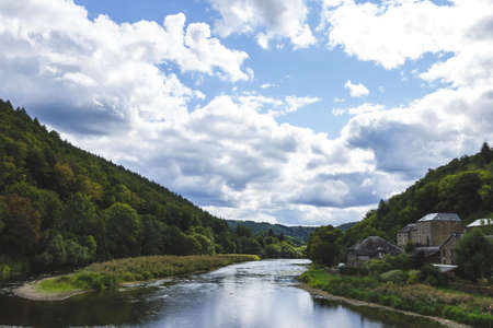 A portrait of the semois river with on one side a small village and on the other a forest and a mountain.の写真素材