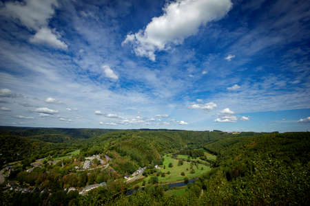 A landscape photograph of the area of LaforÃªt in the ardennes in Belgium with a blue sky and lots of forest. There is a village and the Semois river flowing through the woods.の写真素材