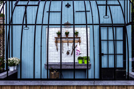 A portrait of an open outdoor gardening shed. The shed is made of a wooden wall and bars like a bird cage. In the shed their are some tools and a beautiful stone sink.の写真素材