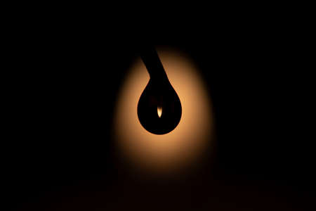 An abstract art portrait of a silhouette of a water drop against the light of a flame of a candle. Inside of the droplet, the flame is refracted upside down.の写真素材