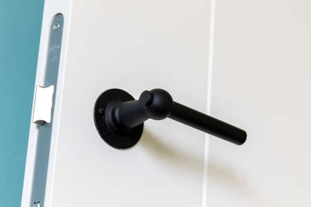 A closeup portrait of a black design doorhandle on a white door. The metal door lock is also visible. On the door there is no keyhole.の写真素材