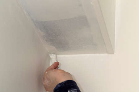 A portrait of a person painting the corner between a wall and the ceiling of a room in a house. The hand of the person is holding a paint brush with a white color on it. The paint is still wet.の写真素材