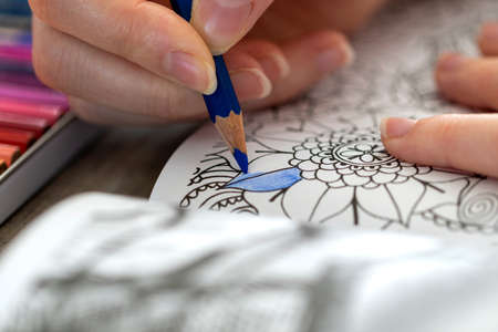 A portrait of a hand of a person holding a blue colored pencil, coloring in a coloring book for...