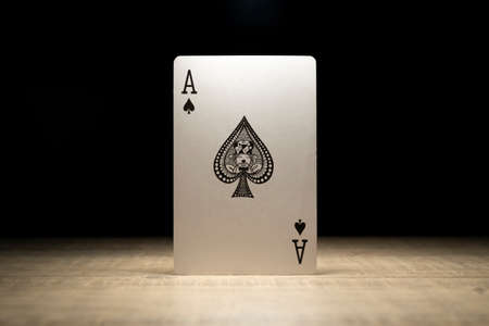Brecht, Belgium - 29 May 2020: A portrait of the ace of spades standing up in the spotlight on a wooden table surrounded in darkness. There are no other playing cards of the deck in the picture.の写真素材