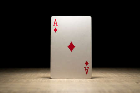 Brecht, Belgium - 29 May 2020: A portrait of the ace of diamonds standing up in the spotlight on a wooden table surrounded in darkness. There are no other playing cards of the deck in the picture.の写真素材