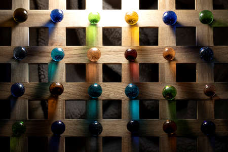 A top down portrait of multiple marbles all having a different color, lying on a wooden roster casting a colorful shadow onto the wooden surface.の写真素材