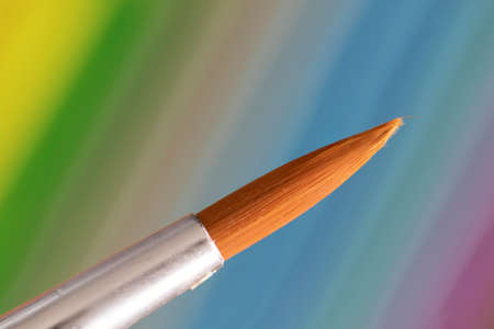 A macro portrait of a paintbrush tip in front of a colorful background. The brush hair is still together forming a nice tip.の写真素材