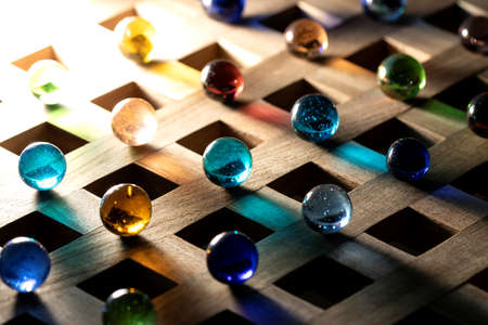 A portrait of multiple marbles all having a different color, lying on a wooden roster casting a colorful shadow onto the wooden surface.の写真素材