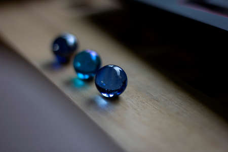 A portrait of three blue marbles, each having another shade of blue, on a wooden surface. Shining a bit of blue light onto the wood.の写真素材