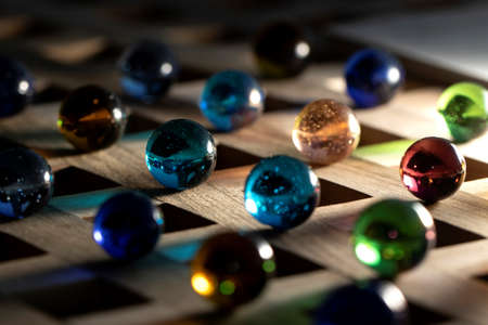 A portrait of a lot of different marbles in different colors, lying on a wooden roster casting a colorful shadow onto the wooden surface.の写真素材