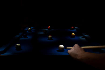 A light painted portrait of a billiard table with lit billiard balls and a person playing the game with a stick. The holes are lit as well.の写真素材