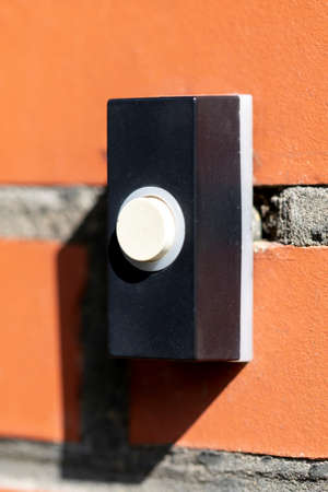 A close up portrait of an old electric doorbell on a red brick wall. The device is black with a white button to ring the bell.の写真素材