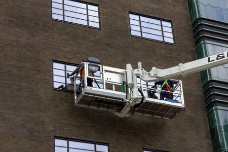 A portrait of two window washers, using a crane to get to the top windows of the building in a big box to do their cleaning job in comfort.のeditorial素材