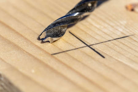 A closeup portrait of a wood drilling bit lying on a wooden plank next to a pencil marking where the carpenter will drill a hole in the piece of wood. The marking is a cross.の写真素材