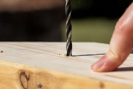 A closeup portrait of a person drilling a hole in a piece of pine wood. The wood drill bit has already cut itself a bit into the wooden plank, there are a few wood chips lying around.の写真素材