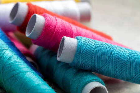 A portrait of three spools of colorful thread lying on some other rolls of fiber. The yarn or wire is ready to be used for a sewing project or some other needle work.の写真素材