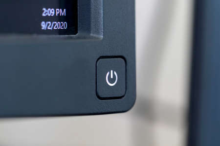 A portrait of the on or off button at the corner of a PC monitor ready to be pressed. The computer screen is on, the light in the symbol of the button is on and the screen is showing some information.の写真素材