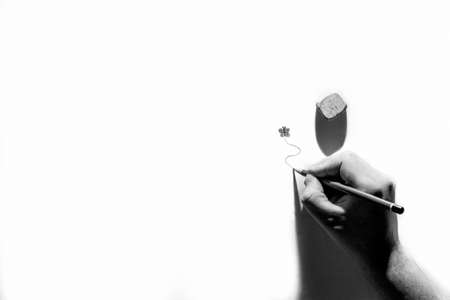 A black and white minimalistic abstract portrait of a hand of a person drawing a swirling line beneath a drawn butterfly using a pencil with a strong shade of a light source.の写真素材