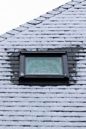 A vertical portrait of a frozen slate roof with a skylight window which is also frozen during winter time. At the sides of the window the frost has molten because of bad isolation.の写真素材