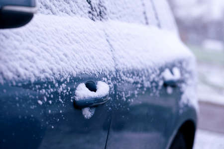 A portrait of the side door handles of a car getting completely snowed under during a snowstorm. The...