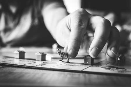 Brecht, Belgium - 28 July 2020: A hand of a person reaching out holding the metal dinosaur pawn or game piece of a game of monopoly between the fingers and placing it on a playing field of the board.のeditorial素材