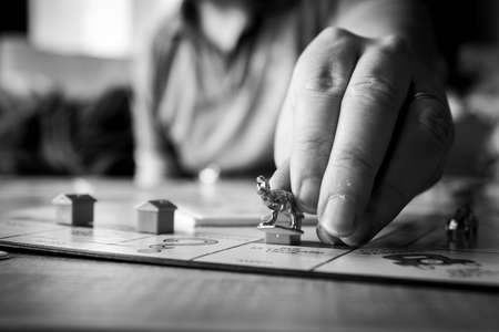 Brecht, Belgium - 28 July 2020: The fingers of a hand of a person reaching out holding the metal dinosaur pawn or game piece of a game of monopoly and placing it on a playing field of the game board.のeditorial素材
