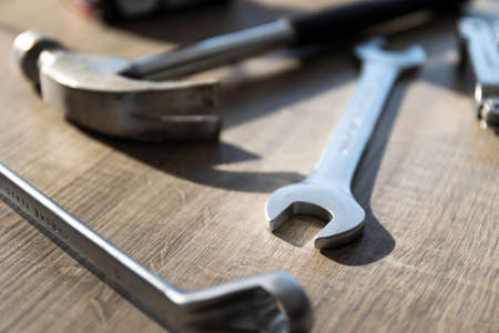 A portrait of a hammer, an open end and a box end wrench lying on a wooden table. The tools are being used to perform a construction task or some kind of repair work.の写真素材