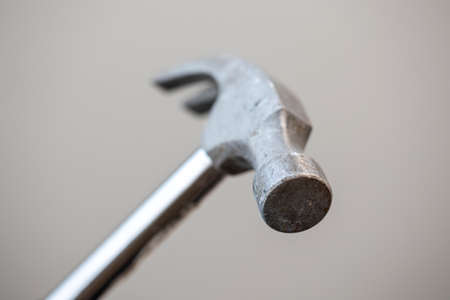 A portrait of the top part of a metal claw hammer isolated on a gray background. The tool is a bit worn by using it for work in construction.の写真素材