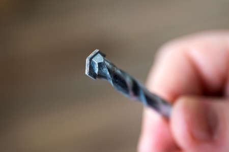 A closeup portrait of a hand of a person holding a stone drill bit. The high speed steel metal tool is spiral shaped and is used in a drilling machine to drill holes in walls.の写真素材
