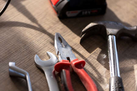 A portrait of a few tools lying on a wooden table. There are pliers, an open and box end wrench and a claw hammer on it waiting to be used for a construction, build or repair job.の写真素材