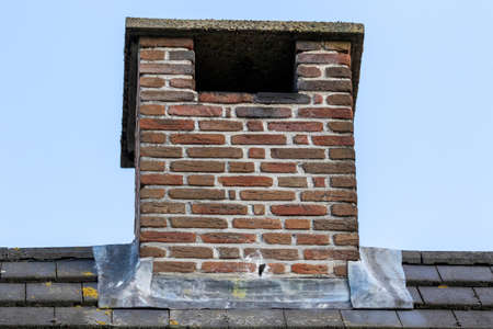 An isolated portrait of a small masonry grout red brick chimney on a black tile roof on an overvast day.の写真素材