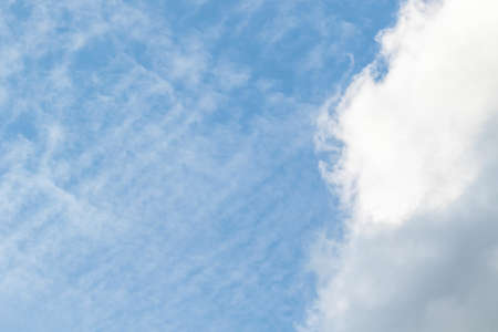 A portrait of a vibrant blue sky with some fibratus clouds and a normal cloud on a sunny day.の写真素材