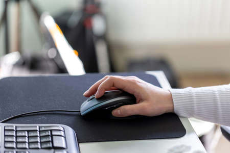 A person holding and using an optical computer mouse to navigate on screen. The peripheral device is moved around on a mousepad to scroll or browse through applications or internet websites.の写真素材