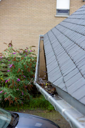 A portrait of a roof gutter full of water because it is clogged due to small branches and fallen leaves due to autumn or fall season. A yearly maintenance chore to stop flooding and water damage.の写真素材