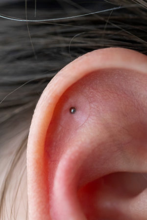 A close up portrait of the ear of a woman with acupressure ear seed in it. The single metal balls...