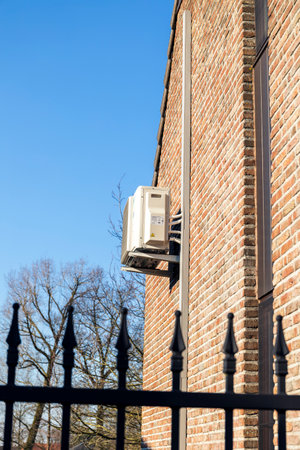 Brecht,Belgium - March 4 2022: An air conditioning unit hanging outside of a building on a brick wall, to regulate the temperature indoors. The cooling system is installed high up on the house.のeditorial素材
