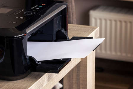 A portrait of a printer with a blank white piece of paper in its printed output tray. The empty page can be used to display some print out.の写真素材