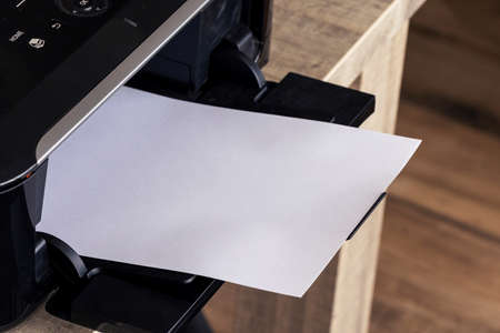 A close up portrait of a printer with an empty white piece of paper in its printed output tray. The blank page can be used to display some print out.の写真素材